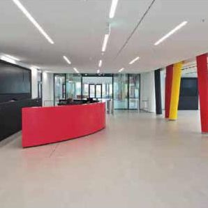 Die Fliesen sind in einem hellen, neutralen Beigeton gehalten, der dem Raum Weite verleiht und die farbigen Akzente der Säulen und des Tresens (in den klassischen Goldbären-Farben) besonders gut zur Geltung bringt.